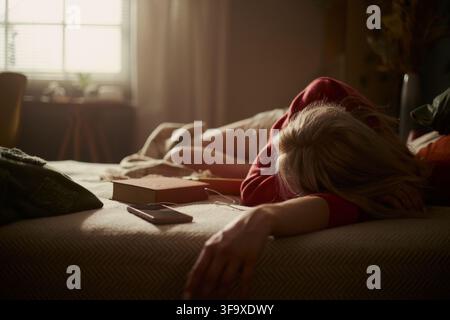 Caucasian young woman lying face down on bed feeling exhausted and depressed. Concept of mental burnout and fatigue, suitable for healthcare and wellness campaigns, eye level shot Stock Photo