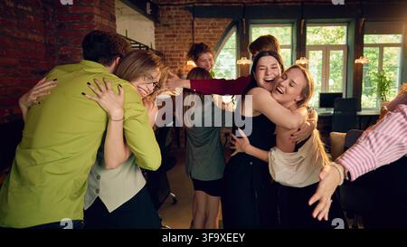 Office colleagues hugging and celebrating together after joyful company event Stock Photo