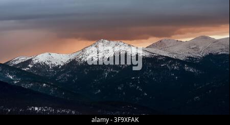 Snow covered mountain peaks under stormy sunset sky Stock Photo