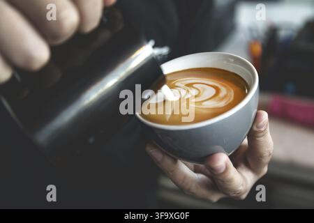Barista preparing cafe latte, pouring milk into a coffee. Closeup on latte art. Stock Photo