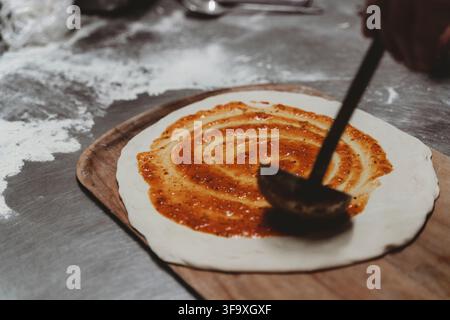 Chef spreading tomato sauce on pizza dough Stock Photo