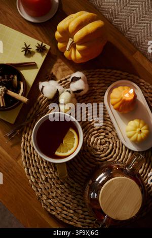 High angle view of autumn tea setting with orange slice in mug, pumpkin, and burning candle on wooden table. Perfect for seasonal marketing, wellness blogs, and cozy lifestyle content, vertical Stock Photo