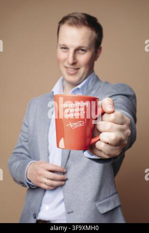 Studio portrait of determined successful businessman in suit and shirt holding red mug with positive slogan Everything is under control . He is smilin Stock Photo