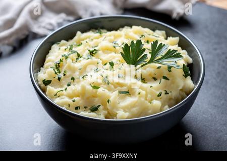 Bowl of creamy homemade mashed potatoes garnished with fresh parsley on a dark background Stock Photo