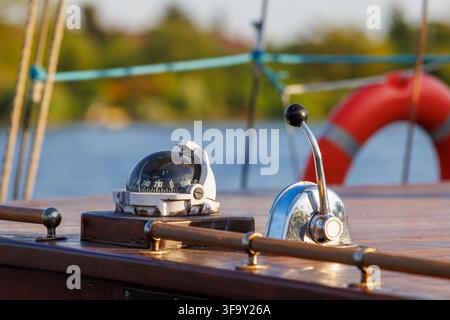 A close-up view of a boat's control station featuring a vintage compass and a shiny metal control lever on a polished wood surface. A red lifebuoy and Stock Photo