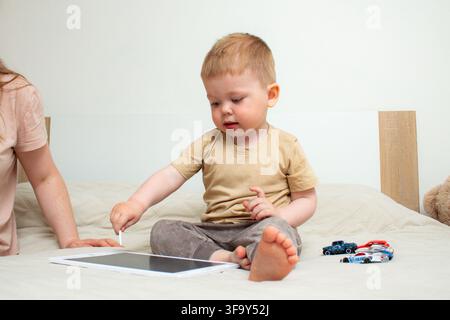 Mother and two year old son drawing on kids tablet with stylus. Parent child bonding through creative play. Fine motor skills developing while making Stock Photo