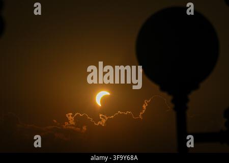 View of a partial solar eclipse partially obscured by clouds with the silhouette of a street lamp in the foreground in Turin, Piedmont, Italy. Stock Photo