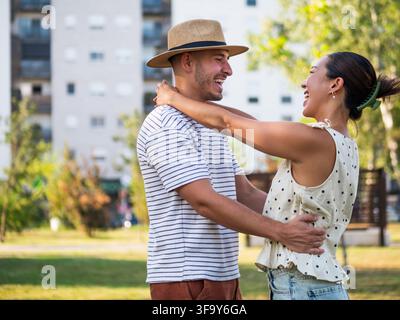 Happy young couple embracing and laughing together during a romantic moment in a sunny park. Stock Photo