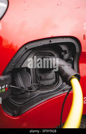 Close-up of a charging plug connected to a red EV in rainy Norway in late summer, symbolizing electrification and humanity’s move beyond fossil fuels Stock Photo
