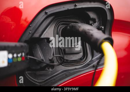 Close-up of a charging plug connected to a red EV in rainy Norway in late summer, symbolizing electrification and humanity’s move beyond fossil fuels Stock Photo