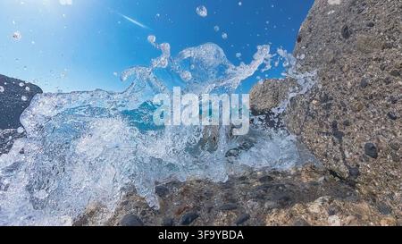 A wave crashes against a rock with splashes of water and foam in the foreground Stock Photo