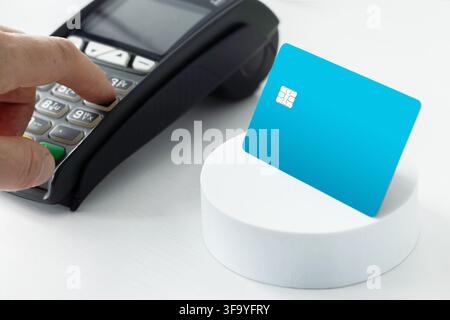 Close-up of a hand entering a PIN code on a payment terminal keypad next to a blue credit card on a stand, representing secure banking transactions an Stock Photo