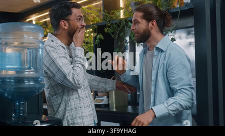Diverse two happy men laughing with unbelievable news Caucasian man whispering secret whisper funny news to Indian Arabian guy laugh friends coworkers Stock Photo