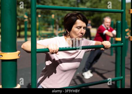 Mature woman doing push-ups from the crossbar on outdoor sports ground Stock Photo