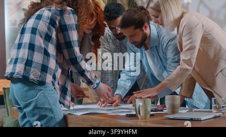 Casual informal business team designers architects emotional discussing blueprint building project plan in office five partners discuss talking job Stock Photo