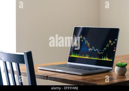 Laptop displaying trading chart on wooden table. Financial technology in a simple workspace. Stock Photo