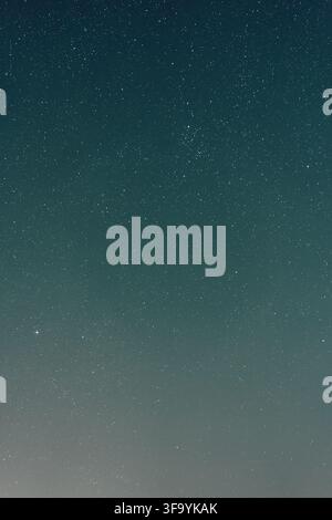 Star filled night sky above faint glowing horizon with teal blue gradient, scattered white points of light, calm dark atmosphere, minimal light Stock Photo
