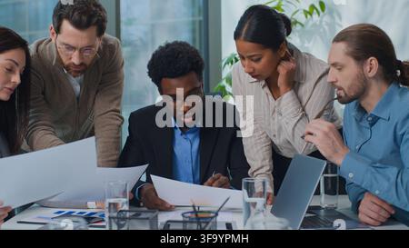 African American businessman boss with multiethnic business team discussing papers stats at office meeting. Five diversity managers talking Stock Photo