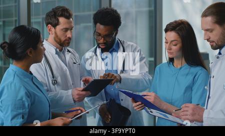 Team five multiethnic doctors talking analyzing patient lung x-ray checkup with digital tablet online medicine service in modern clinic. African Stock Photo