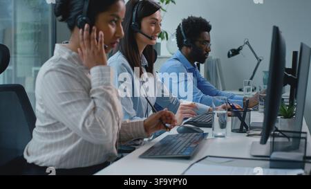 Three busy concentrated multiethnic business colleagues working in call center communicating with clients writing notes in company. Group team of Stock Photo