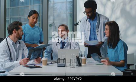 Puzzled multiracial five doctors hesitate thinking talking discussing papers health results x-ray treatment together at medicine briefing. Diversity Stock Photo