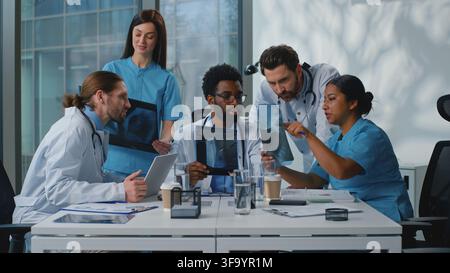 Group team of five multiethnic doctors talking working with x-rays at table at medicine conference. Multiracial medical therapists work with health Stock Photo