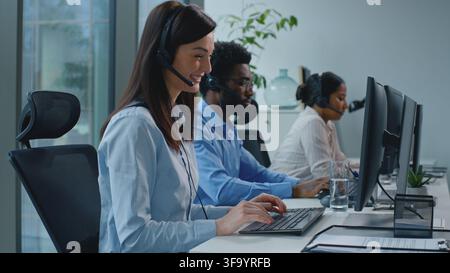 Smiling Caucasian businesswoman working in call center with multiethnic operators business colleagues team talking helpline with headset computer Stock Photo