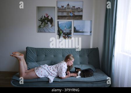 Young woman spending quality time with her domestic cat while resting comfortably on sofa. Stock Photo