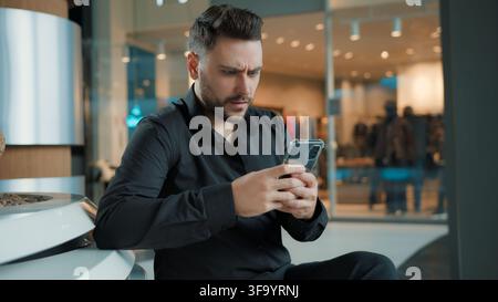 Serious Caucasian man with mobile phone reading news worried at business center businessman male guy with smartphone worry anxiety read message Stock Photo