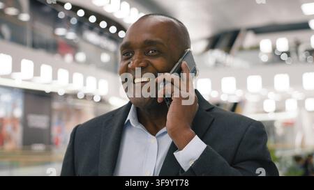 Close up serious African American mature business man talking mobile phone walking male client communicating with smartphone walk in shopping mall Stock Photo