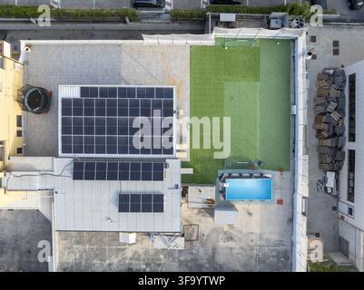 Aerial view of a rooftop featuring a large array of solar panels, a small artificial grass area, and a swimming pool in Fermo, Marche, Italy. Stock Photo