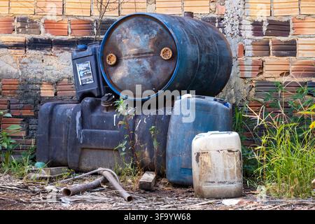 Huge blue plastic gallons and barrels resting against a brick wall Stock Photo
