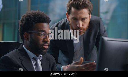 Two multiethnic business men looking in computer monitor and digital tablet serious discuss talk diversity businessmen males partners with online Stock Photo