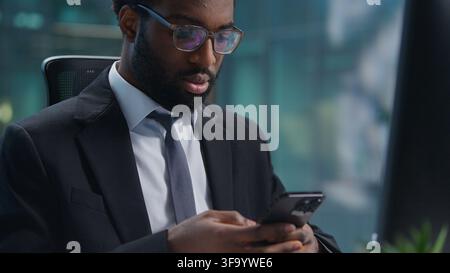 Multitasking African American business man working with computer chatting mobile phone app at office table. Ethnic serious male businessman Stock Photo