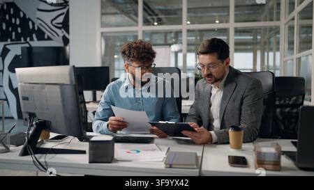 Two concentrated multiethnic business men working with documents discuss financial corporate budget planning income taxes diversity businessmen work Stock Photo