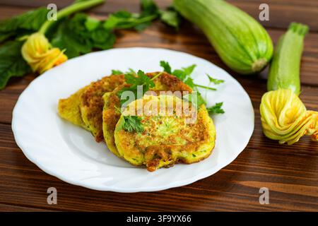 Healthy zucchini pancakes with parsley garnish on white plate and natural background . Stock Photo