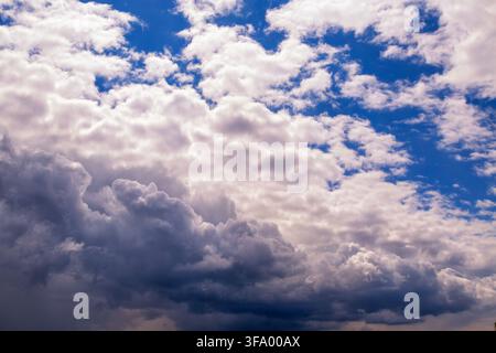 Dramatic horizontal skyscape with dense white and dark cumulus formations floating across vivid blue sky. Stock Photo