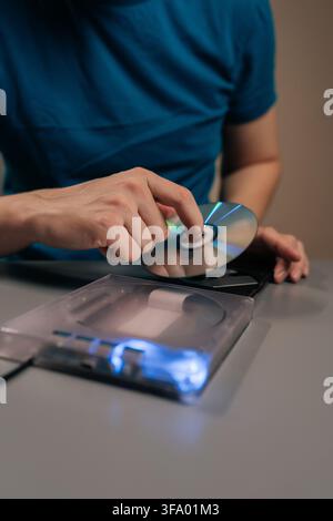 Vertical cropped shot of person interacting with computing hardware, loading data storage disc into portable optical drive, connecting to personal Stock Photo