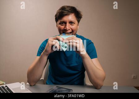 Studio portrait of young man humorously biting data disk, wrapping it in napkin, funny concept of hunger for information and data, with a laptop and Stock Photo