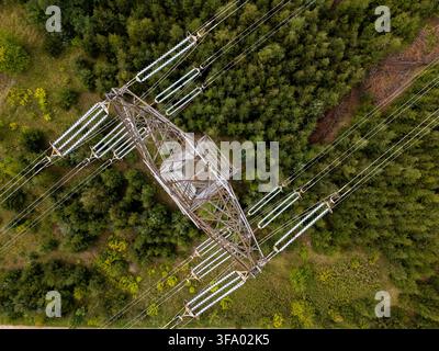 Aerial view of an electricity pylon surrounded by dense green forest with power lines extending across the landscape in Gdansk, Poland. Stock Photo