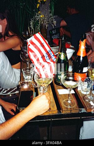 Champagne and prosecco on a crowded café garden table filled with glasses and popcorn, captured with direct analog flash in a lively setting. Stock Photo