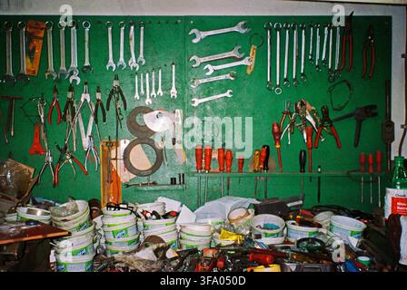 Old tools arranged on a green metal surface in a long-used workshop, with a chaotic workbench in front, captured with direct analog flash. Stock Photo
