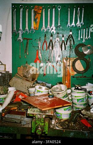Old tools arranged on a green metal surface in a long-used workshop, with a chaotic workbench in front, captured with direct analog flash. Stock Photo