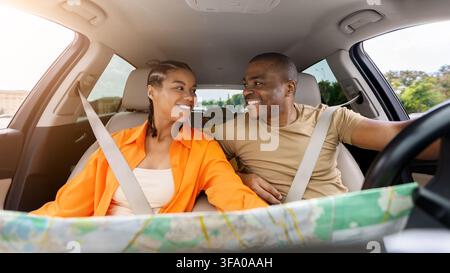 Black couple wearing seat belts and smiling at each other inside car Stock Photo