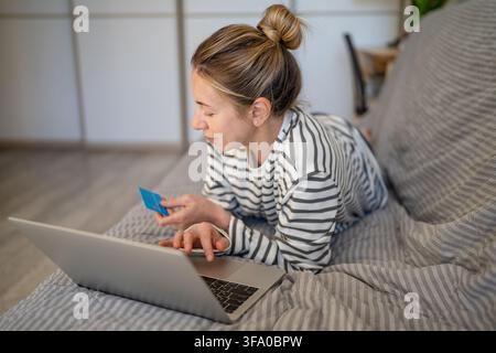Carefree relaxed woman lying on sofa at home shopping online on laptop using bank credit card. Stock Photo