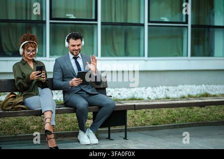 Business colleagues using digital devices and headphones on a bench Stock Photo