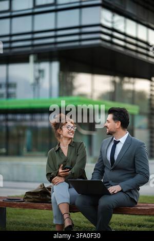 Business colleagues collaborating outdoors on laptop and smartphone Stock Photo