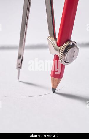metal drawing compass sketching circle on white paper, drafting instrument with red pencil in macro close-up view, architectural engineering Stock Photo
