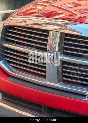 Close-up of red truck front grille with chrome accents. Metal bars arranged vertically on shiny surface. Reflections visible on polished finish. No an Stock Photo