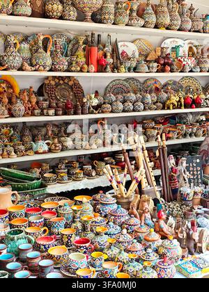 Shelves packed with colorful ceramic pottery and handmade crafts. Brightly painted cups, plates, and figurines fill every surface. Traditional pottery Stock Photo